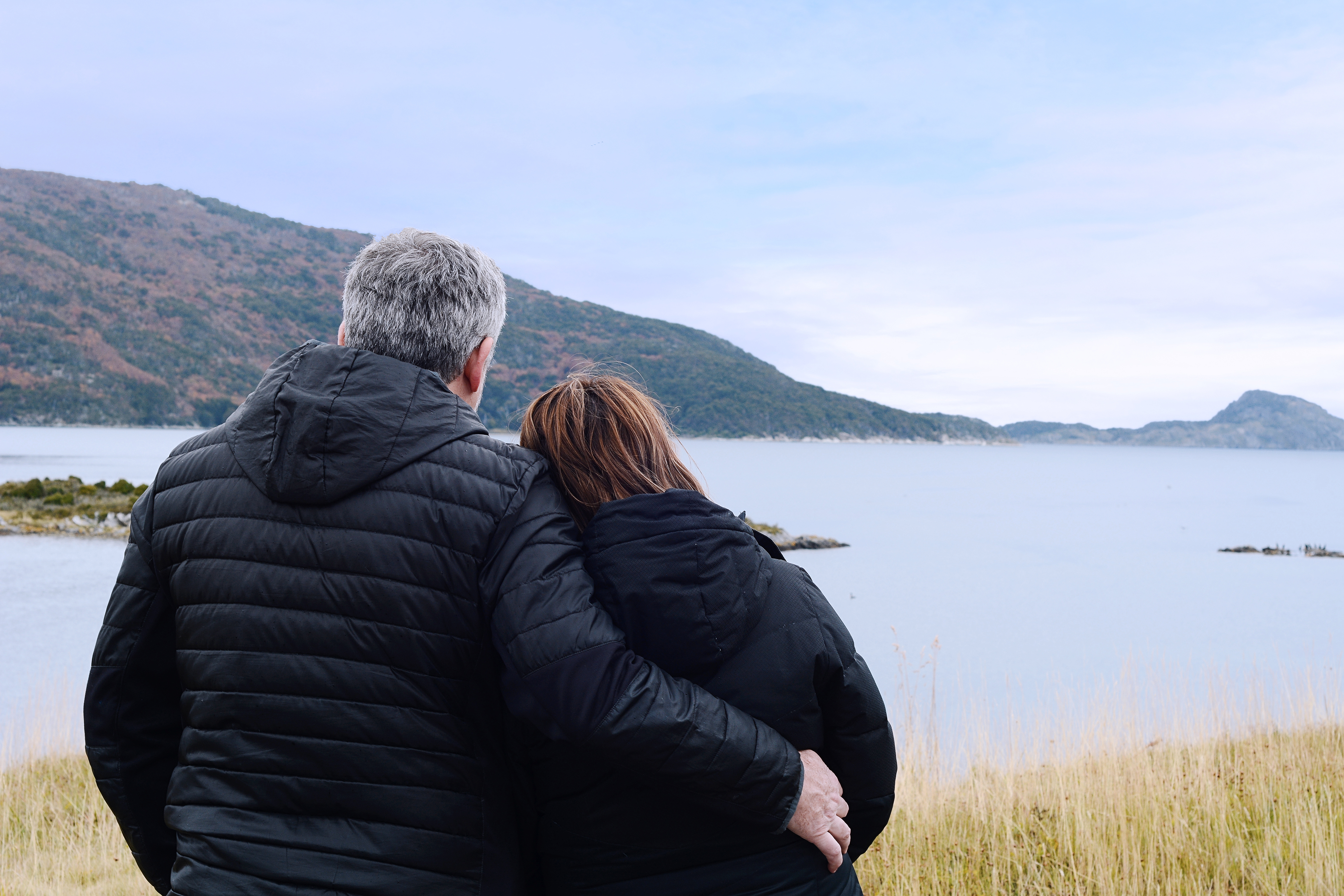 A couple embracing, each holding a rolled-up yoga mat